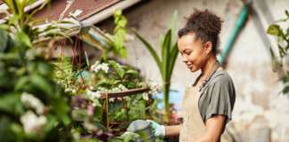 Save It; Don’t Waste It – Tip No. 5 Happy young biracial woman in apron watering garden flowers
